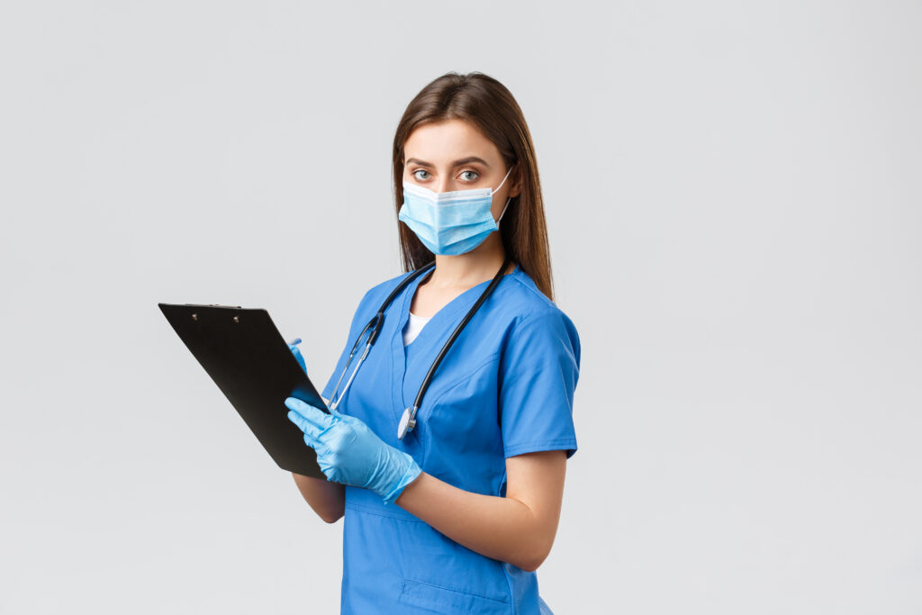 covid 19, preventing virus, health, healthcare workers and quarantine concept. professional female nurse or doctor in blue scrubs, medical mask and gloves, writing down patient info using clipboard