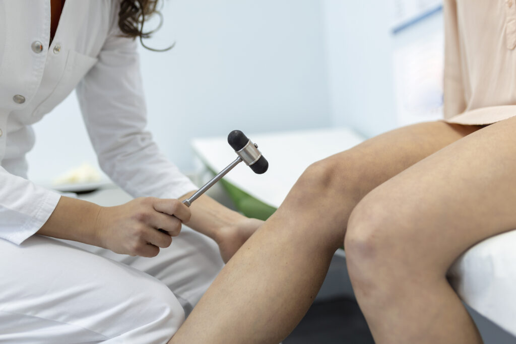 doctor neurologist knocking on knee of patient with hammer in clinic closeup. diagnosis of neurological pathology of knee reflex concept