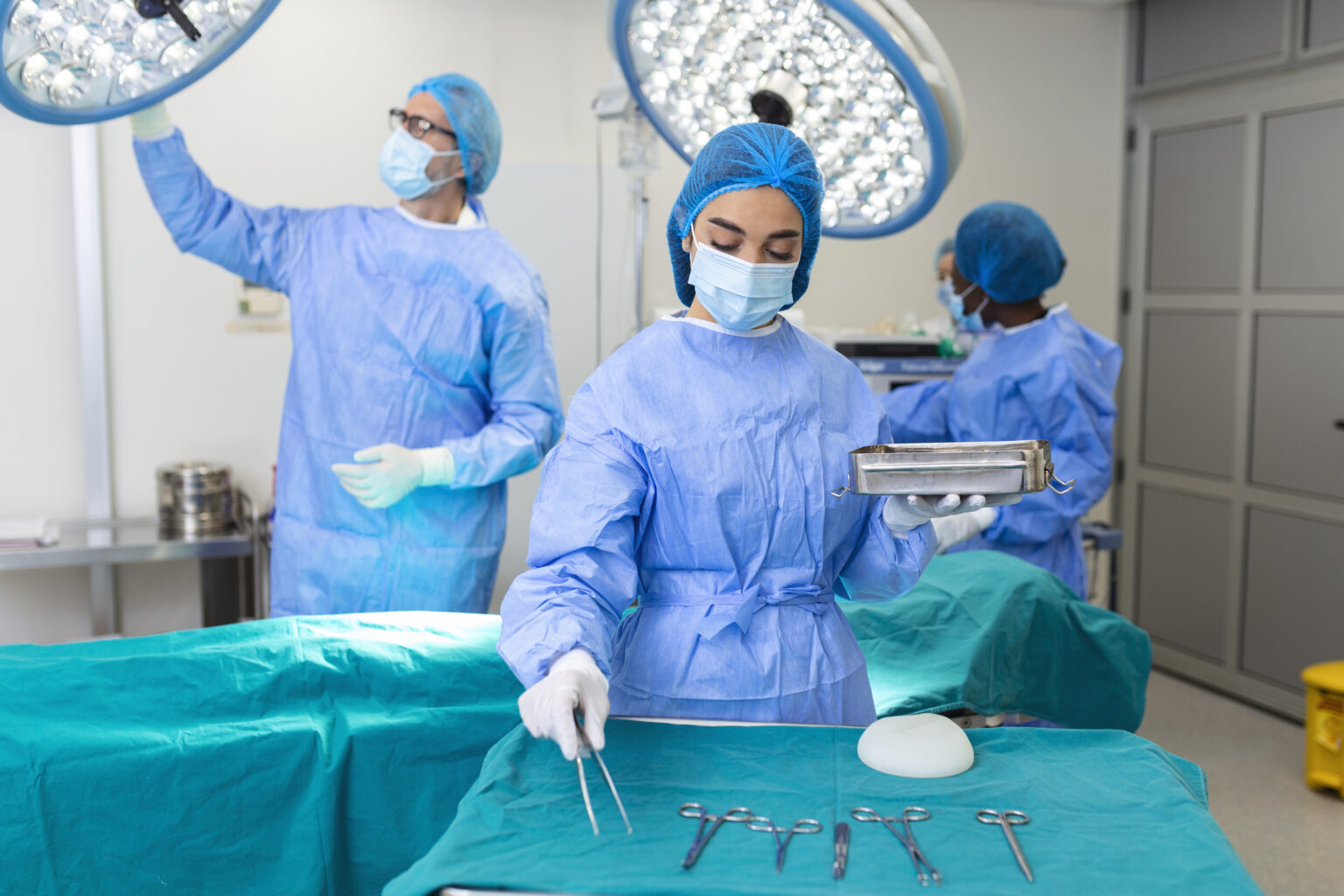 female surgeon in surgical uniform taking surgical instruments at operating room. young woman doctor in hospital operation theater