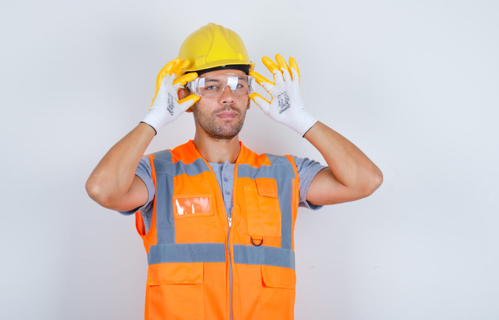 male builder in uniform, helmet, gloves wearing safety glasses , front view.